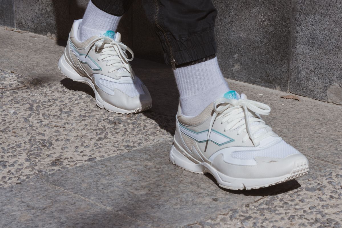 Person in white sneakers walking along a city pavement