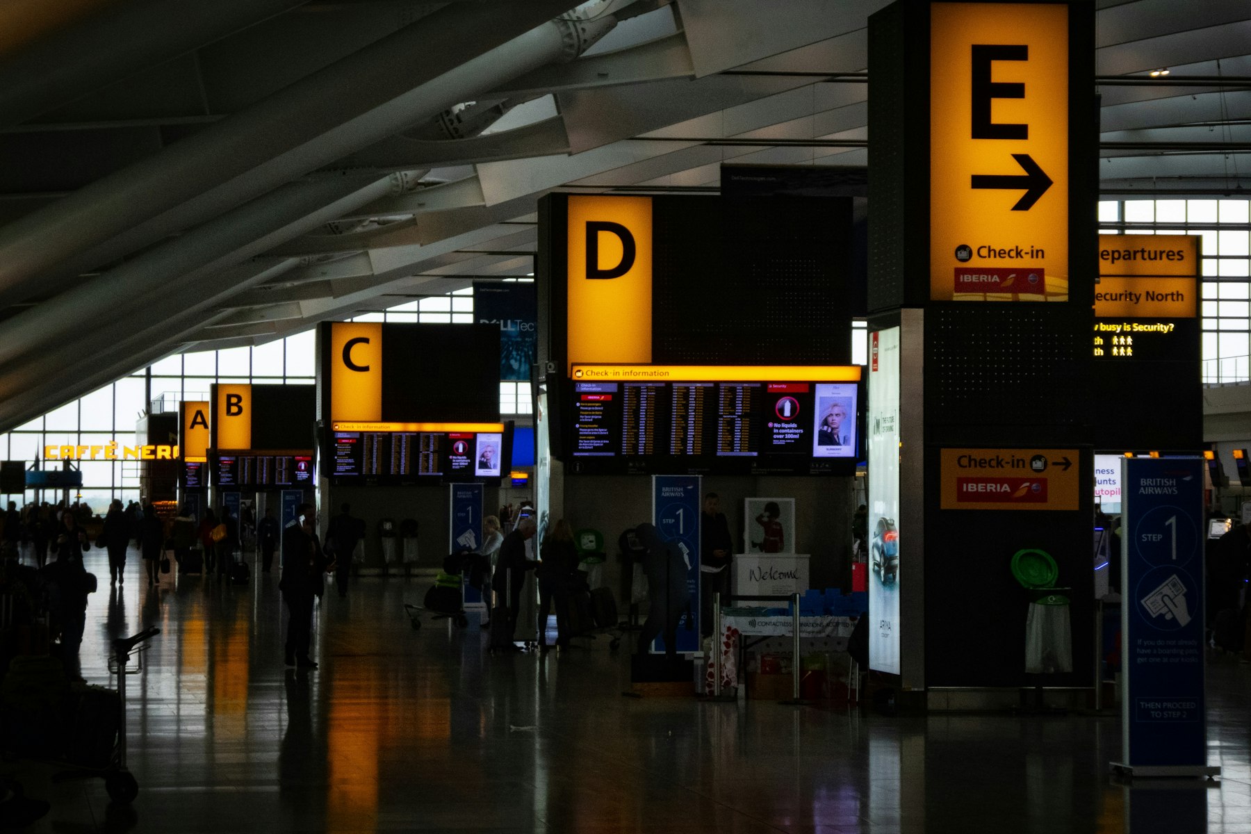 An airport check-in hall lit by amber wayfinding signs, with polished terrazzo floors underfoot
